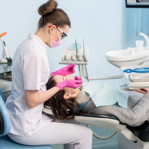 Female dentist with dental tools - mirror and probe checking up patient teeth at dental clinic office. Medicine, dentistry and health care concept. Dental equipment